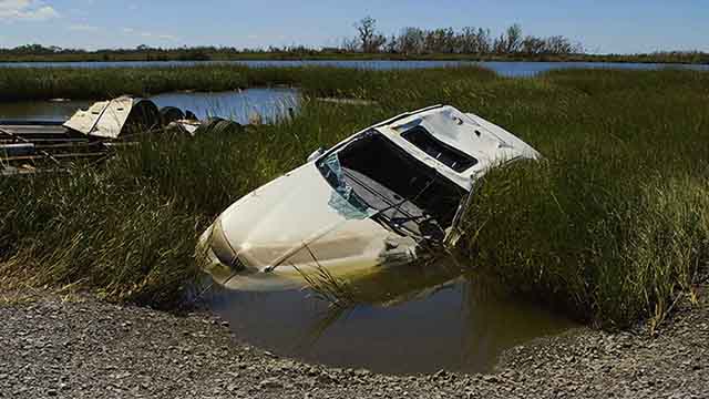 Photograph of a car half-submerged in a marsh, in the aftermath of a hurricane.